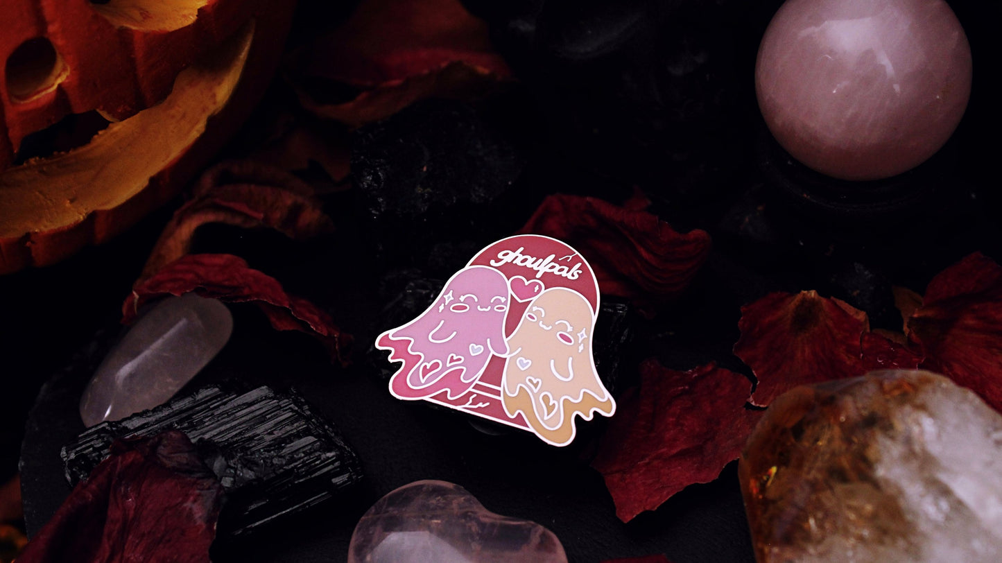 Ghoulpals Lesbian Pin - Silver plated enamel pin of two cute and smiling ghosts holding hands in front a tombstone that says "ghoulpals" with a heart in between them, in the colours of the lesbian flag which is orange, pink, and magenta. Original design by GRRRL Spells.