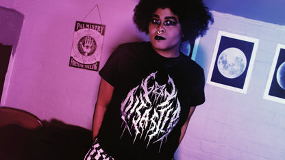 Gay Disaster Shirt - A person wearing a black t-shirt with the words "Gay Disaster" in a black metal style front printed on it in silver metallic ink. the A in "Gay" is shaped like an inverted pentagram. Original design by GRRRL Spells. 