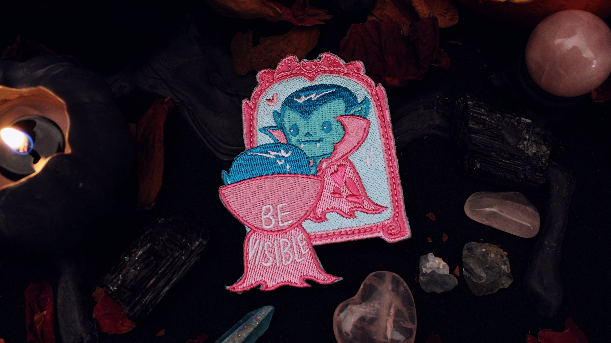 Be Visible Patch - Iron on embroidered patch of a cute vampire looking at their reflection in a mirror, in the trans flag colours of blue, pink, and white. The words Be Visible are seen on the back of their cape. Original design by GRRRL Spells. 