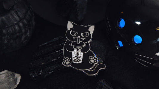 Black Cat Boba Pin - Silver plated enamel pin of a cute black cat sitting upright with a little smirk on its face while sipping on a cup of bubble tea/boba with moon and stars in it. Original design by GRRRL Spells.