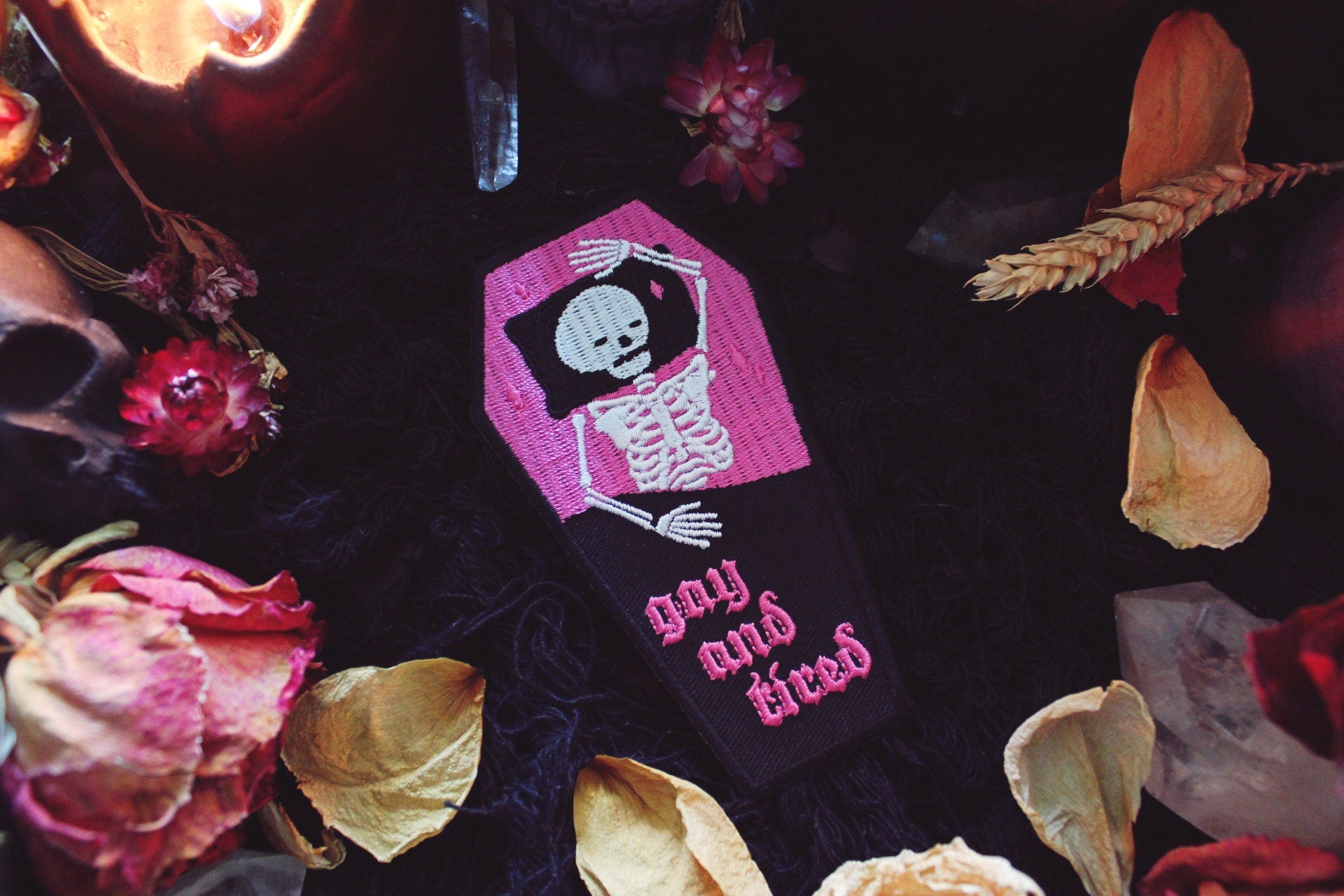 Iron on embroidered patch that is coffin shaped with black border and half pink on the top and half black on the bottom as background. Skeleton lays in the coffin bed exhausted as the words "gay and tired" in lowercase letters written on the bottom half of the coffin in gothic typography. Original design by GRRRL Spells. 