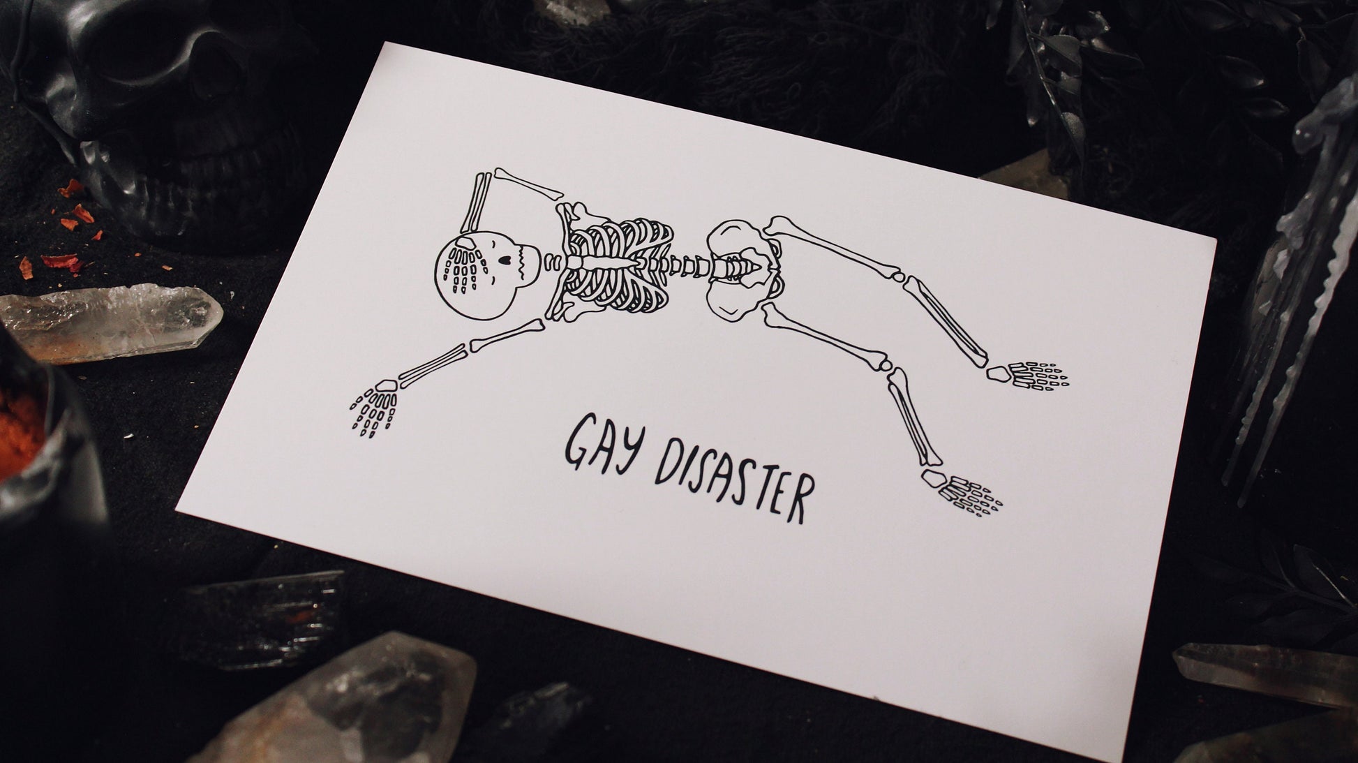 Gay Disaster Print - Illustration of a skeleton laying horizontally with one hand over their forehead and another hand splayed out on the side, on a white background with the words "Gay Disaster" at the bottom. Printed on 8.5" x 5.5" card stock. Original design by GRRRL Spells. 